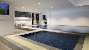 Ein moderner Innenpool mit klarem Wasser, gefliestem Boden und einer Sitzecke mit Stühlen.