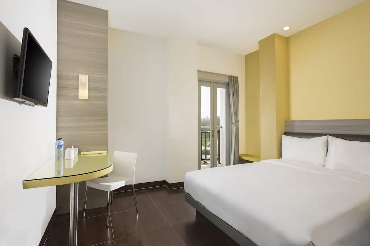 Ein Hotelzimmer mit Bett, Wandfernseher, kleinem Tisch mit Stuhl und einem Vorhangfenster.