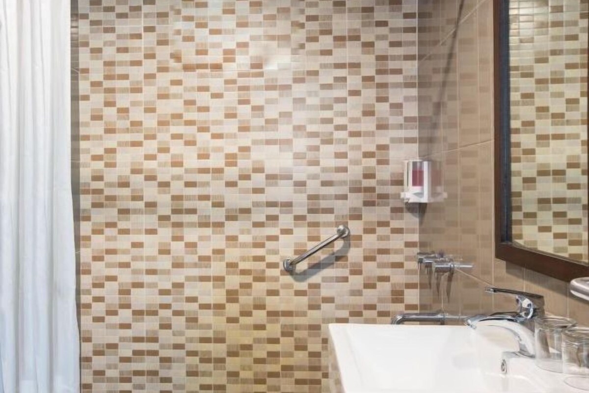 A bathroom with a tiled mosaic wall, a sink with a mirror, and a handheld showerhead.
