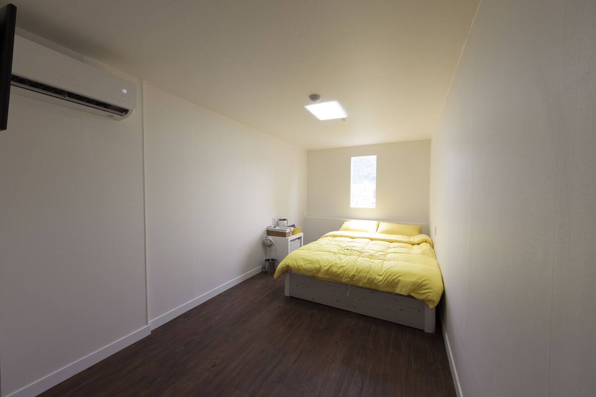 A bedroom with a bed, a nightstand, a window, and an air conditioning unit.