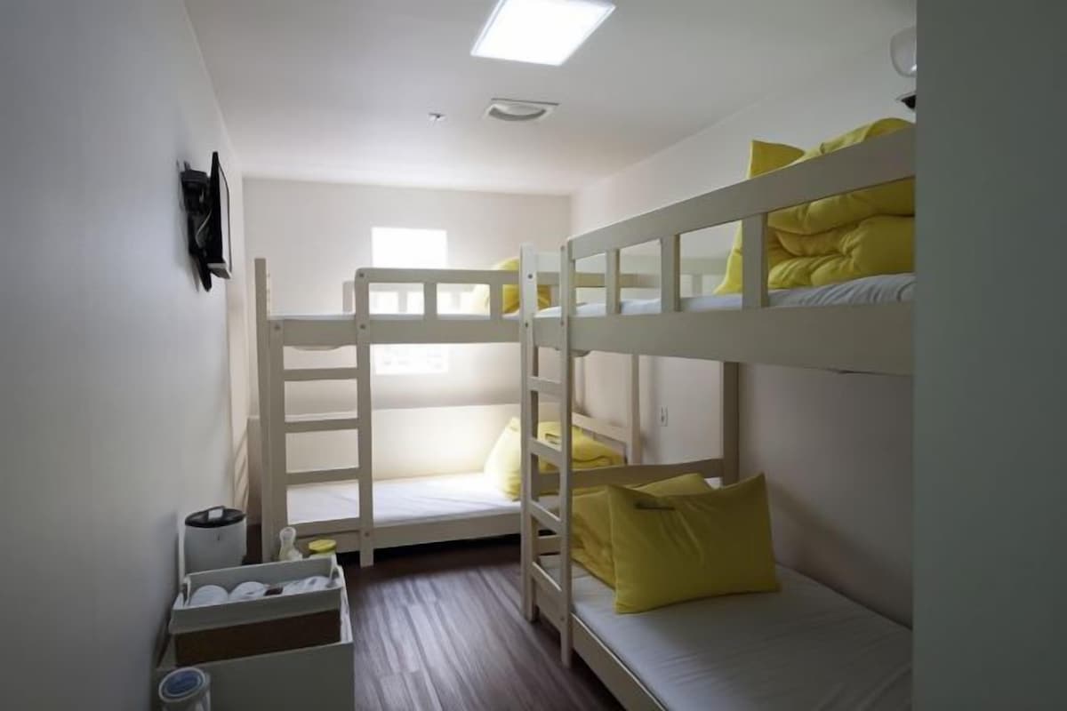 A bunk bed room with white walls, a small window, and a white storage box.