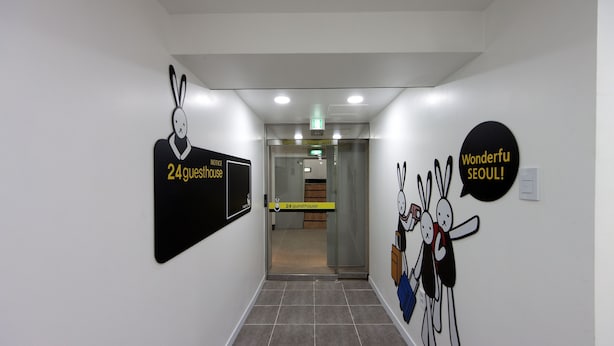 Een gang met een bord dat een 24-uurs pension aangeeft, een deur met een ruit en een muur met een Wonderfu Seoul bord.