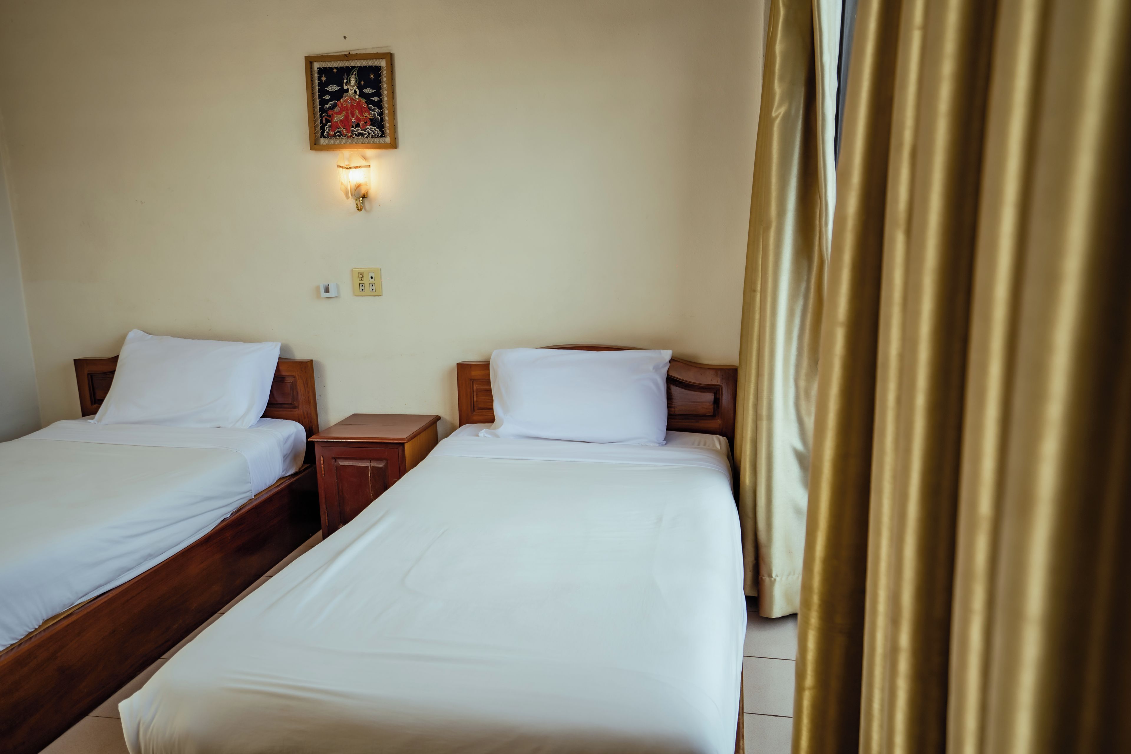 A hotel room with two single beds, a nightstand, a wall-mounted light, and a curtain.