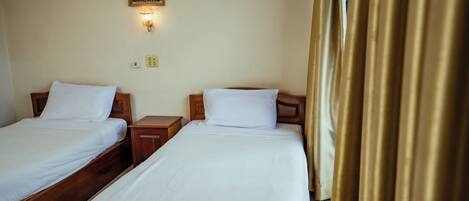 A hotel room with two single beds, a nightstand, a wall-mounted light, and a curtain.