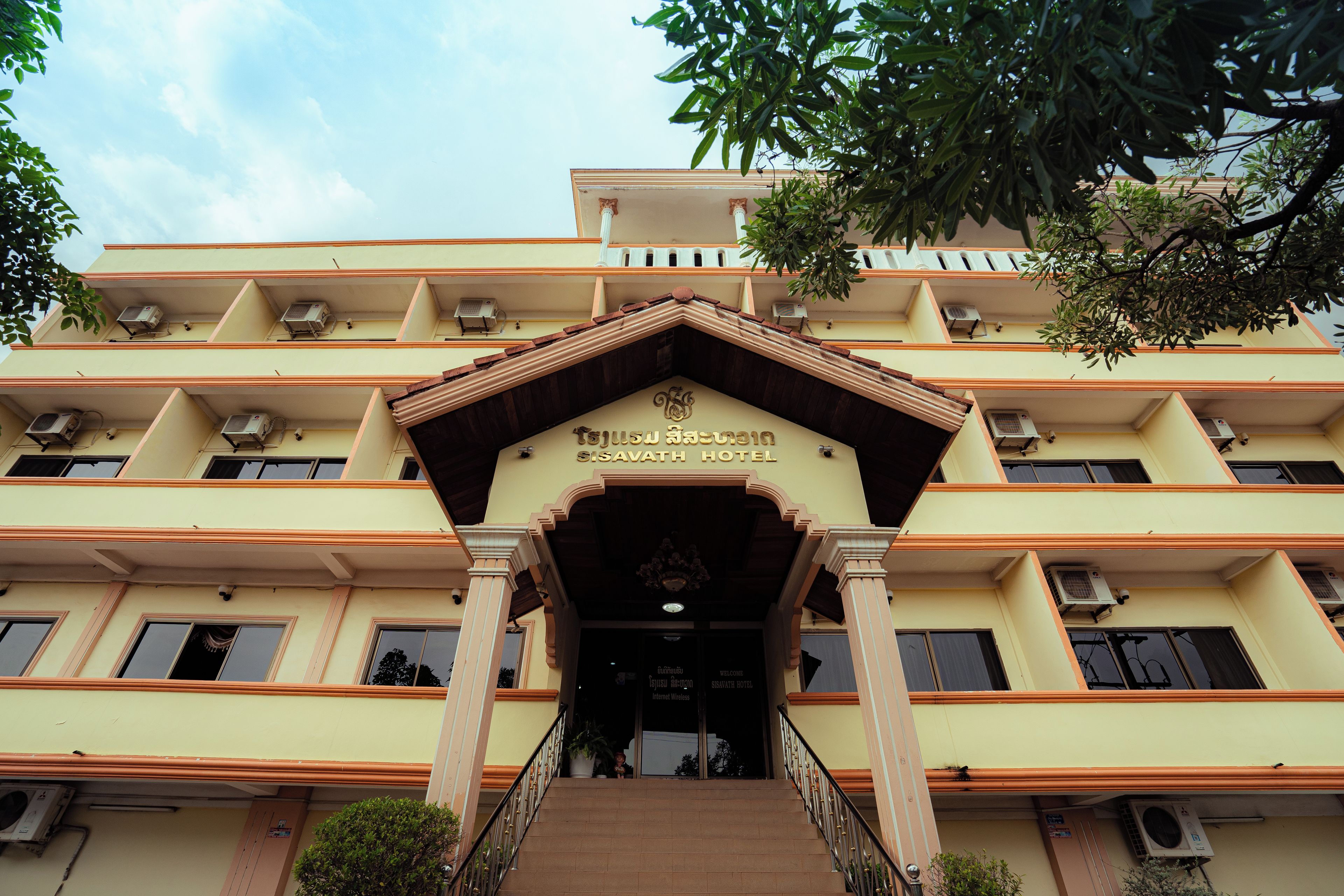 A multi-story building with a central entrance, air conditioning units on each floor, and a sign indicating it is a hotel.