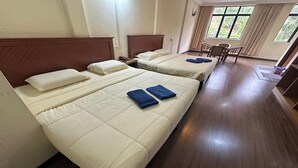 Habitación de hotel con tres camas, cabeceros de madera y un comedor con mesa y sillas.