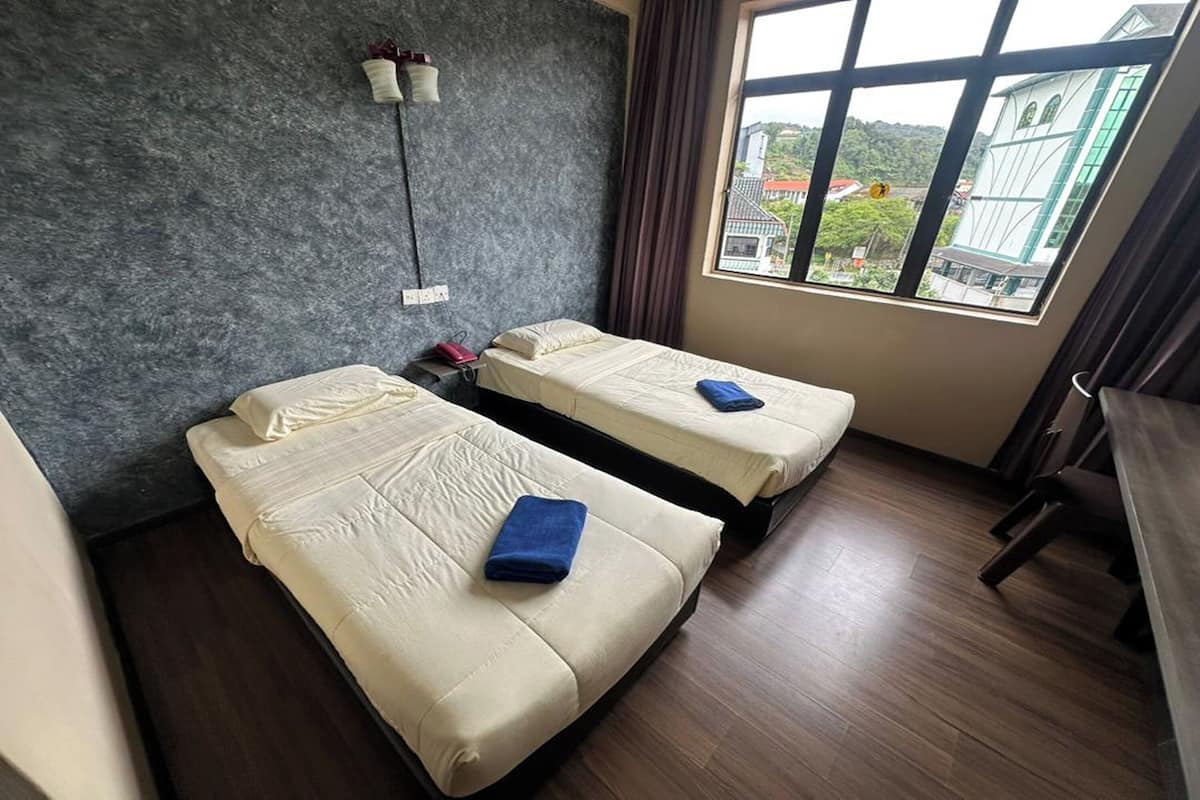 Une chambre d’hôtel avec deux lits, un bureau, une lampe et une fenêtre donnant sur des immeubles.