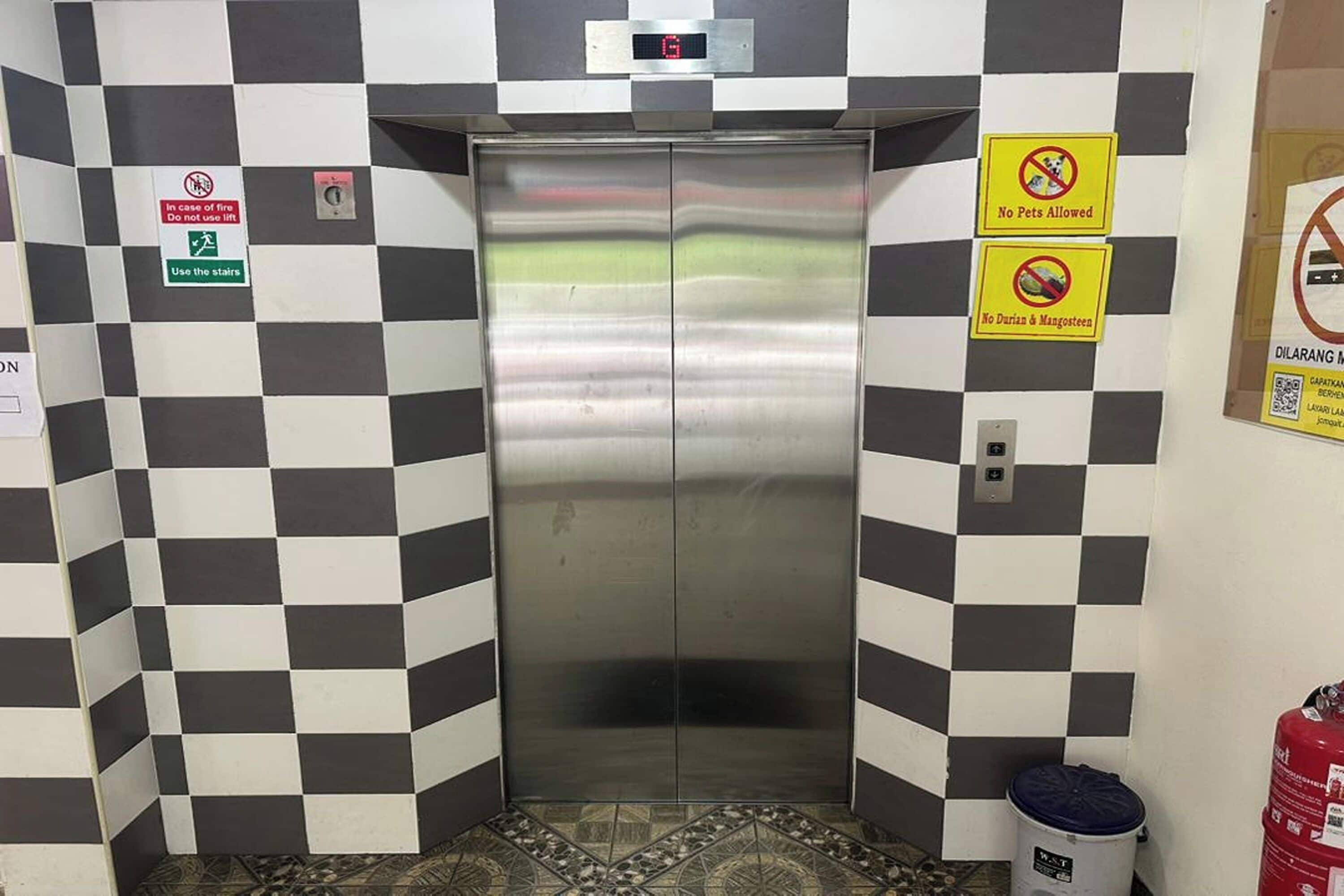 An elevator with a digital display, surrounded by black and white checkered walls, and signs indicating no pets, no dogs, and no wheelchairs allowed.