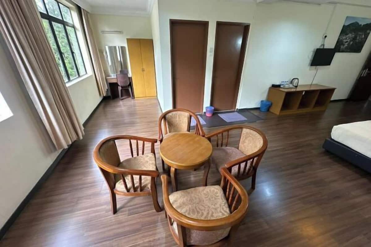 Une chambre d’hôtel avec un plancher en bois, une table ronde entourée de quatre chaises, un lit, un bureau avec une chaise et un téléviseur fixé au mur.