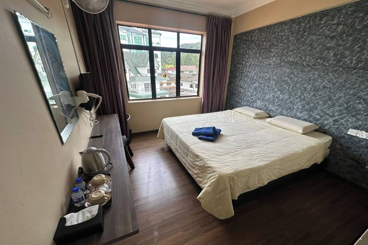 Une chambre d’hôtel avec un grand lit, un bureau avec une chaise, un miroir et une fenêtre avec des rideaux.