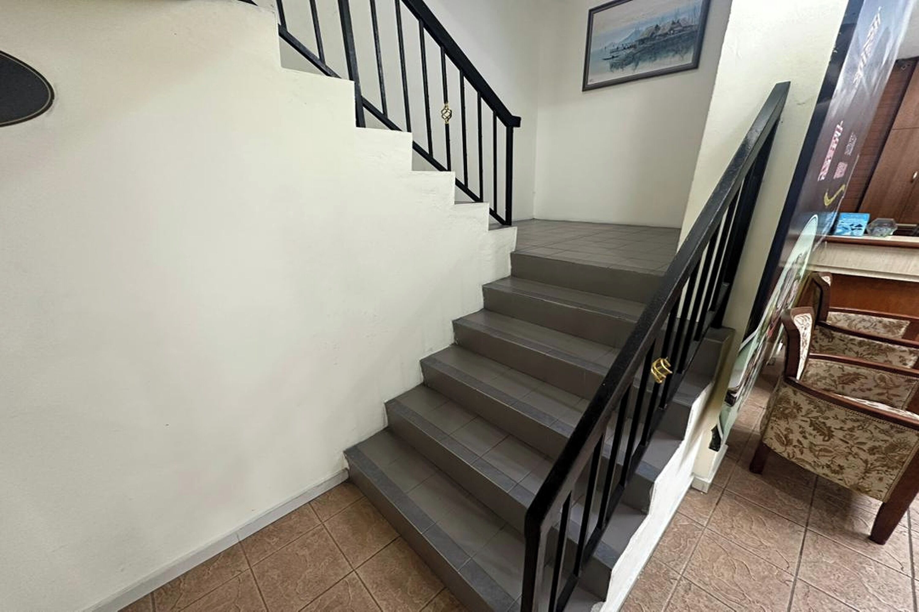 A staircase with a black railing, a wall-mounted picture, and a wooden cabinet with patterned upholstery.