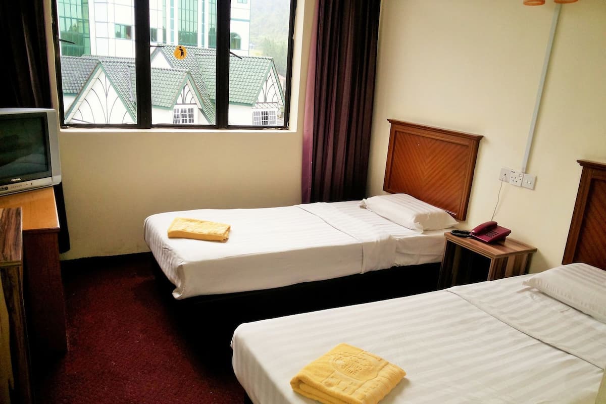 Une chambre d’hôtel avec deux lits, une télévision, un téléphone et une fenêtre donnant sur des immeubles.
