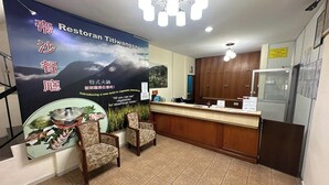 Interior de restaurante con mostrador de recepción, dos sillas, un cartel que anuncia un nuevo plato vegetariano y un letrero que indica la política de registro de entrada y salida.