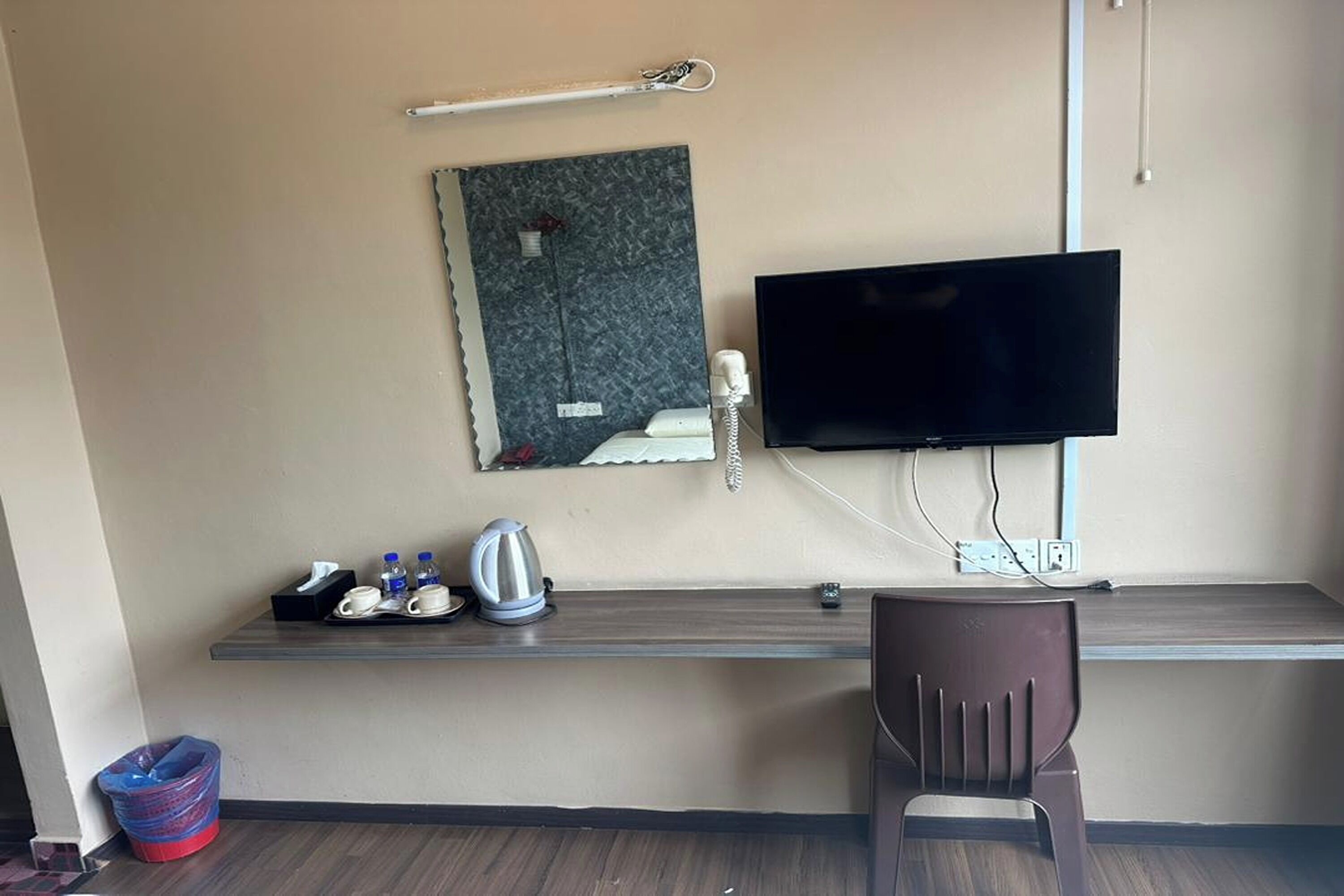 A hotel room with a desk, a television, a telephone, and a small shelf with toiletries.