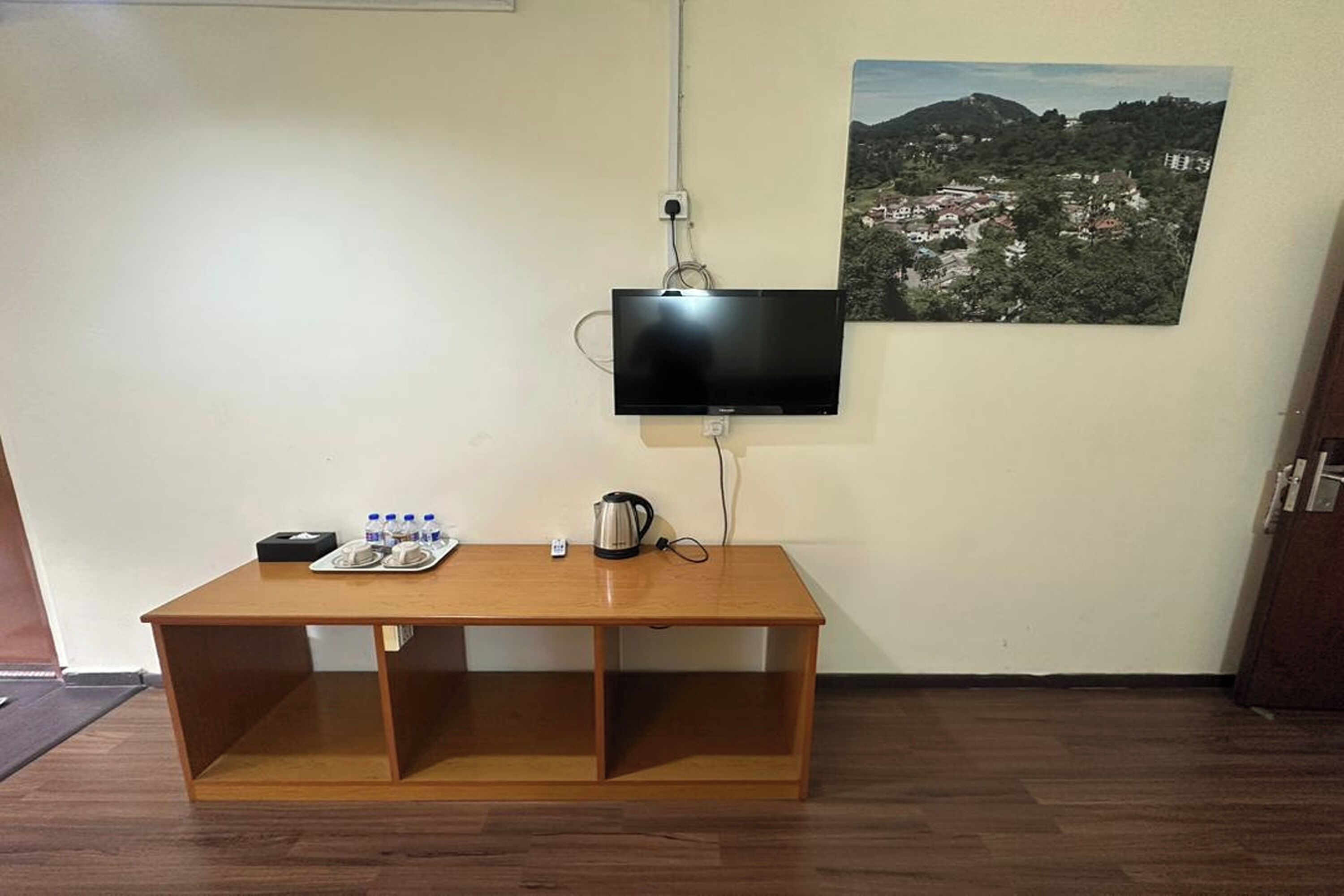 A room with a wooden table, a flat-screen TV mounted on the wall, and a framed landscape picture.