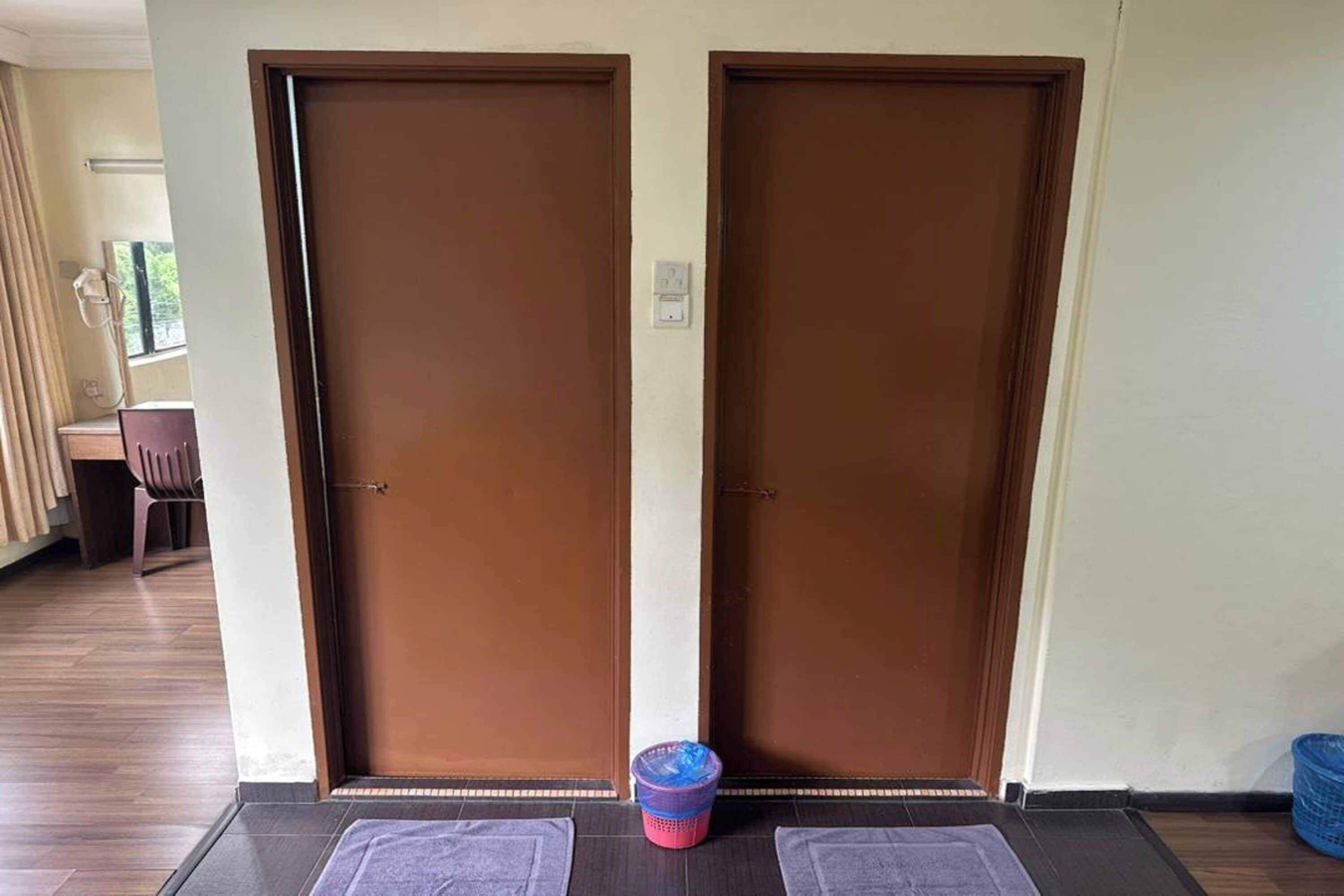 Entrada de hotel con dos puertas marrones, un felpudo y una cesta de plástico en el suelo.