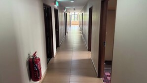Un pasillo largo y estrecho con puertas a ambos lados, un extintor de incendios en la pared y una lámpara en el techo.