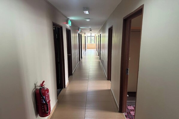 Un pasillo largo y estrecho con puertas a ambos lados, un extintor de incendios en la pared y una lámpara en el techo.