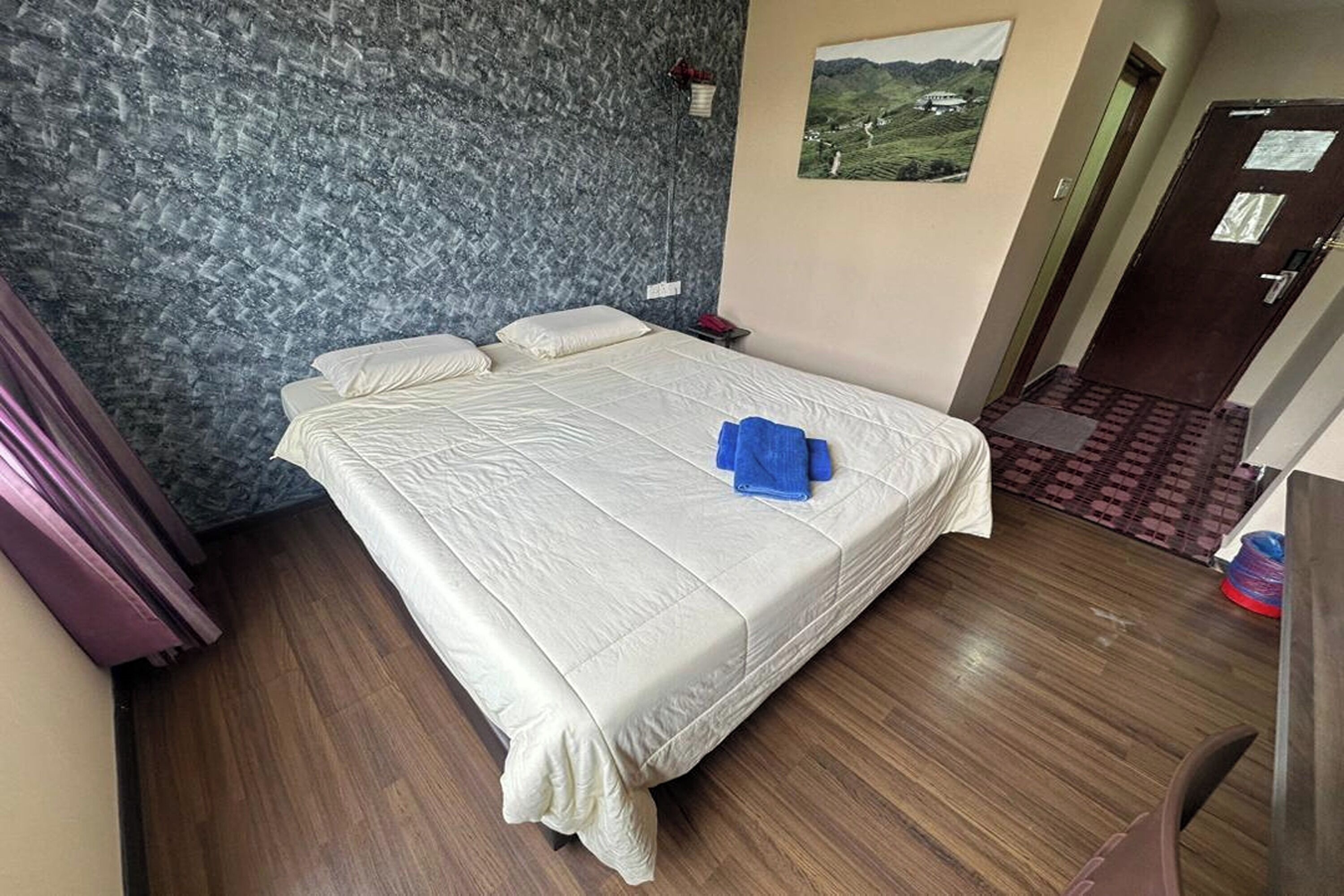 A bedroom with a bed, a nightstand, a wall-mounted lamp, and a door leading to another room.