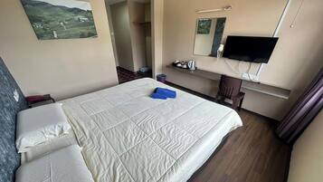A hotel room with a large bed, a desk with a chair, a television, and a painting on the wall.