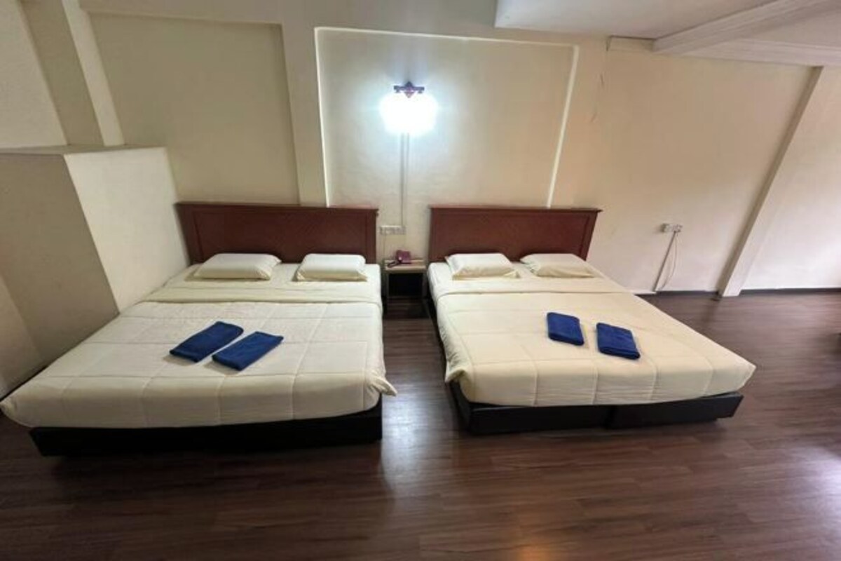 Una habitación de hotel con dos camas individuales, una mesita de noche, una lámpara y suelo de madera.