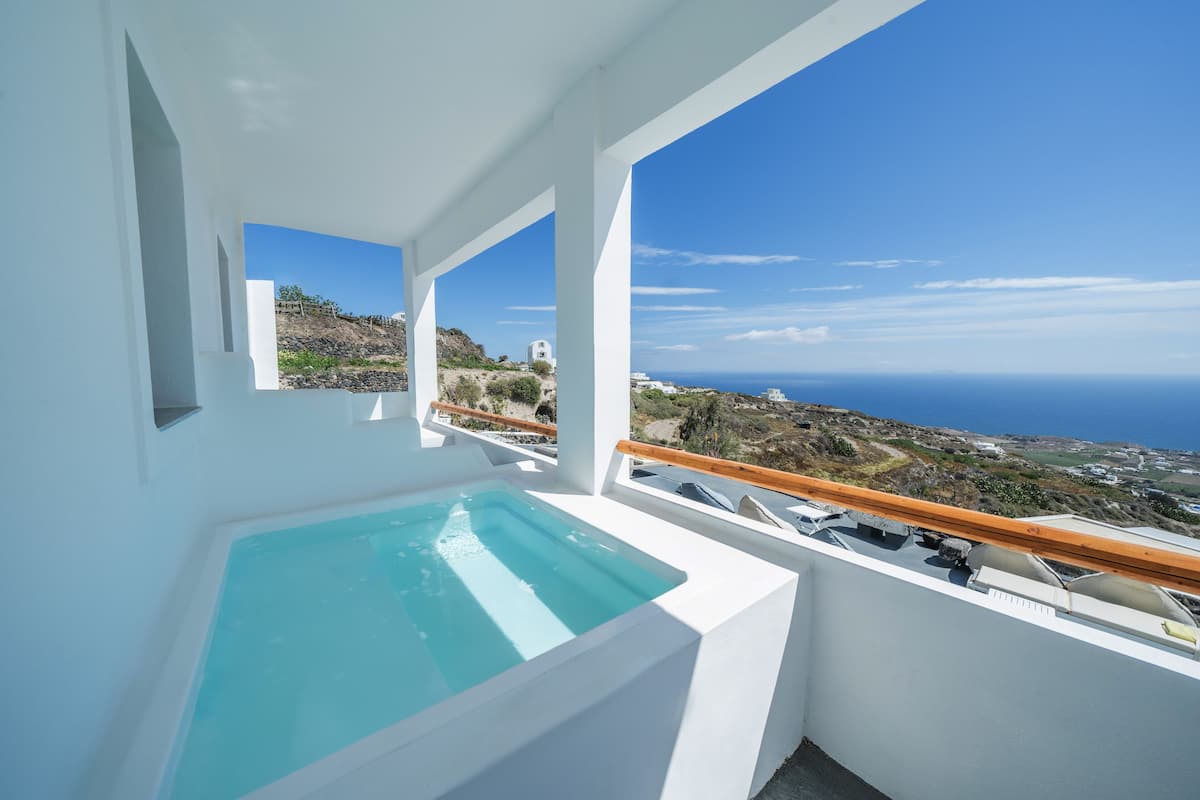 Un balcon moderne doté d’un jacuzzi intégré, de murs blancs et offrant une vue sur la mer et le paysage environnant.