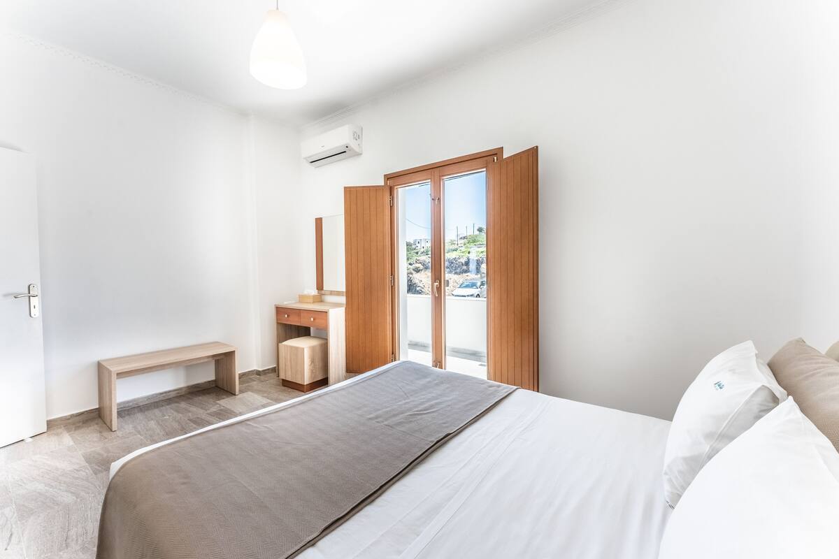 Une chambre à coucher comprenant un lit, un banc, un bureau et une porte coulissante donnant sur l’extérieur.