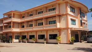 Un hotel de varios pisos con balcones, plantas en macetas y un estacionamiento.