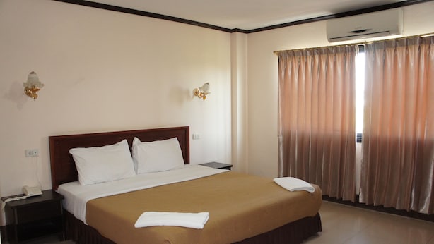 Habitación de hotel con una cama grande, una mesita de noche, un equipo de aire acondicionado y una ventana con cortinas.