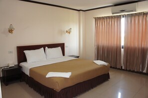 A hotel room with a large bed, a nightstand, an air conditioning unit, and a window with curtains. - Chaleunehoung Hotel (Vientiane)