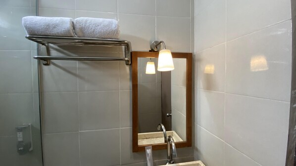 A bathroom with a shower, a towel rack with two towels, a mirror, and a light fixture. - Mawar Asri Hotel (Yogyakarta)