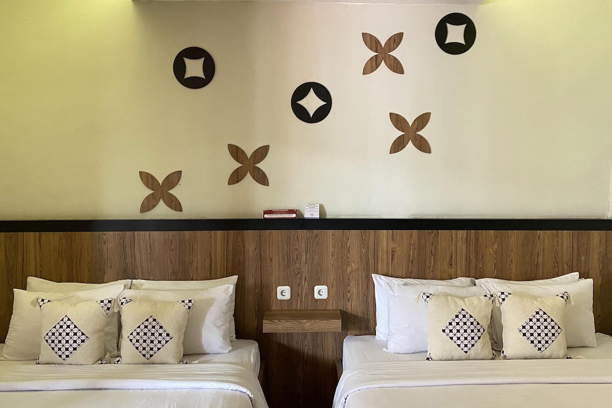 Een hotelkamer met twee bedden, elk voorzien van kussens met een patroon en een houten hoofdbord.