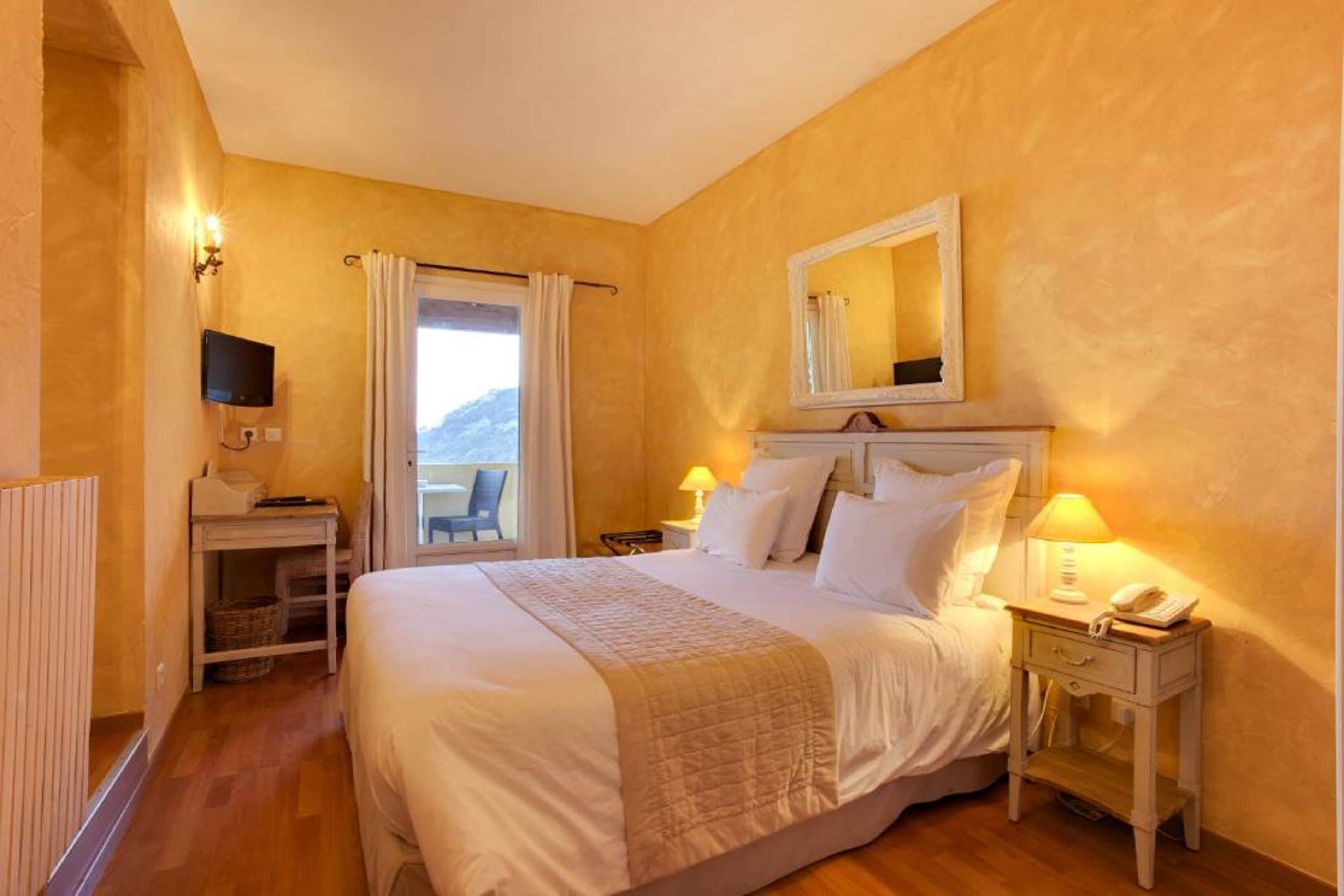 Une chambre d’hôtel équipée d’un lit, de lampes de chevet, d’une télévision, d’une fenêtre avec des rideaux et offrant une vue sur l’extérieur.