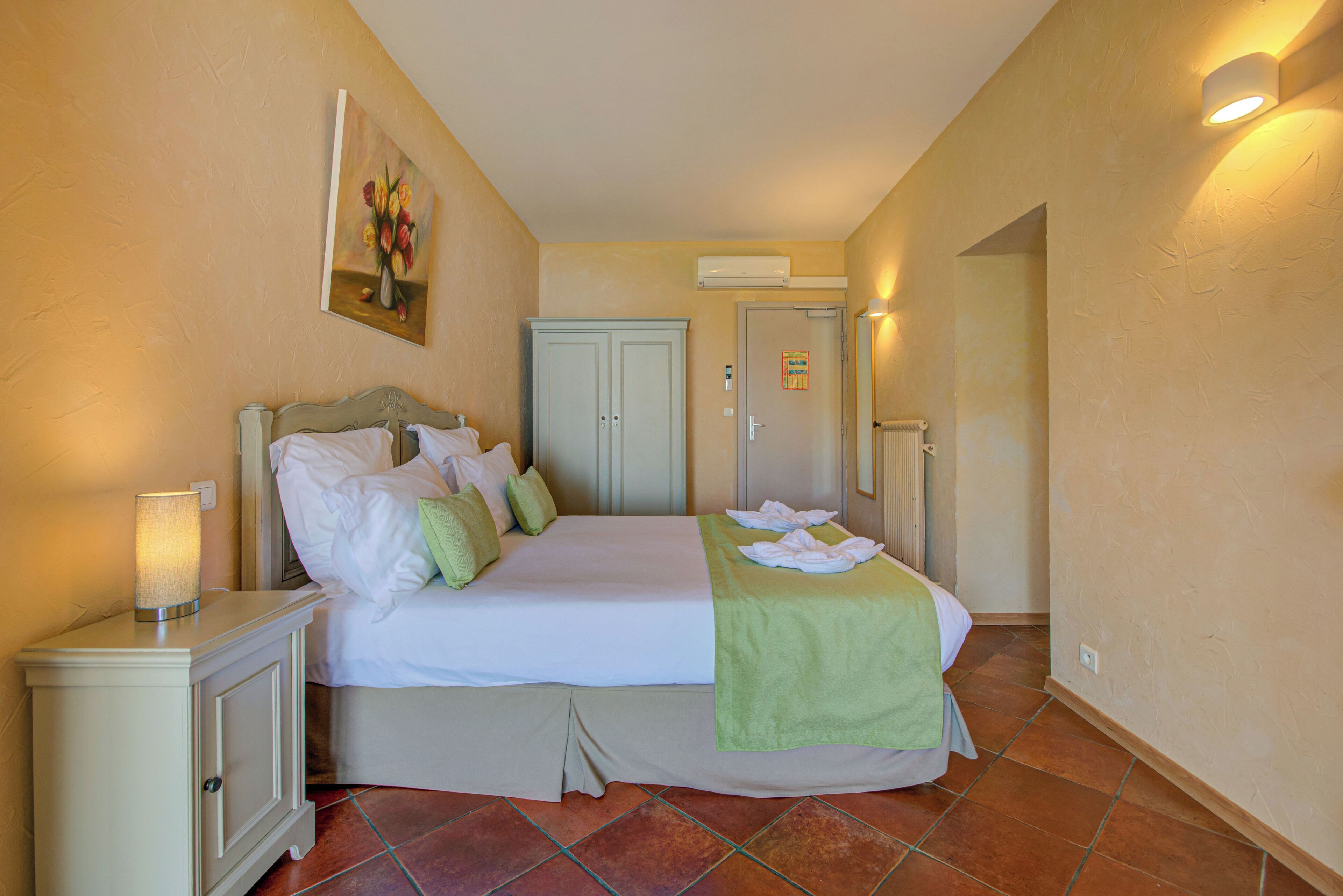 A hotel room with a bed, bedside table, and a painting on the wall.