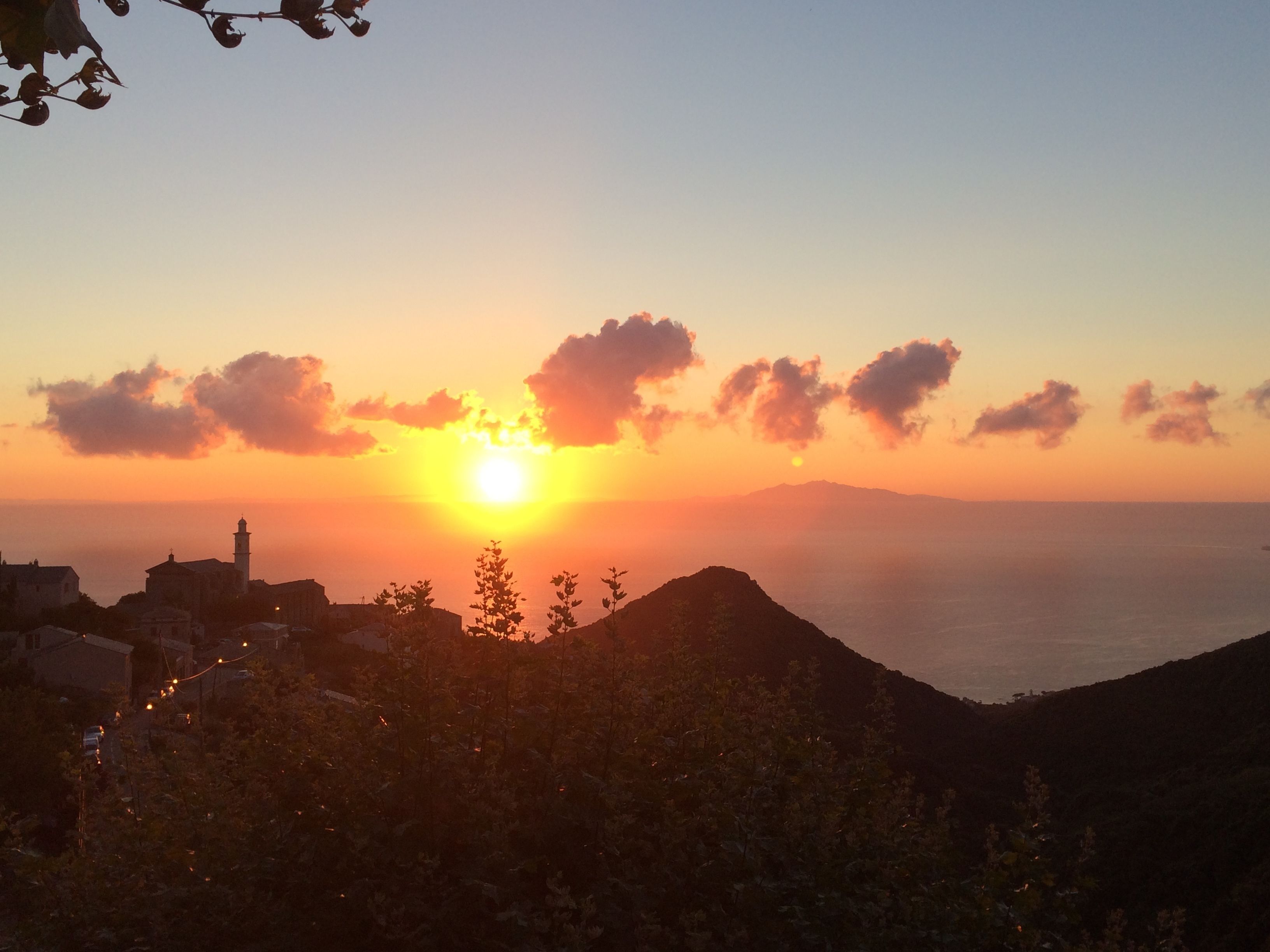 Un coucher de soleil sur une ville côtière, avec ses bâtiments et un imposant beffroi.
