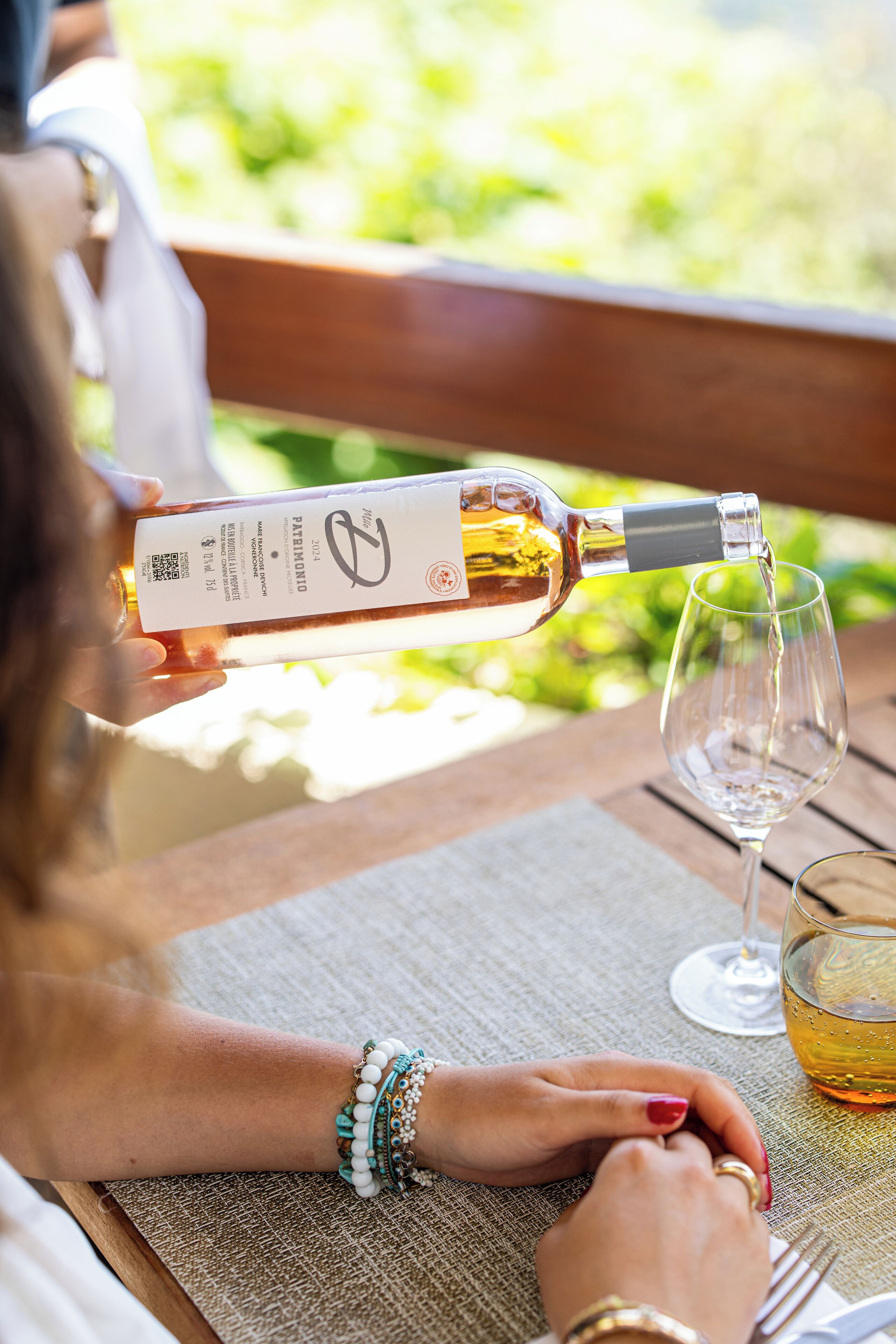 A person pouring wine into a glass at an outdoor table with a placemat.