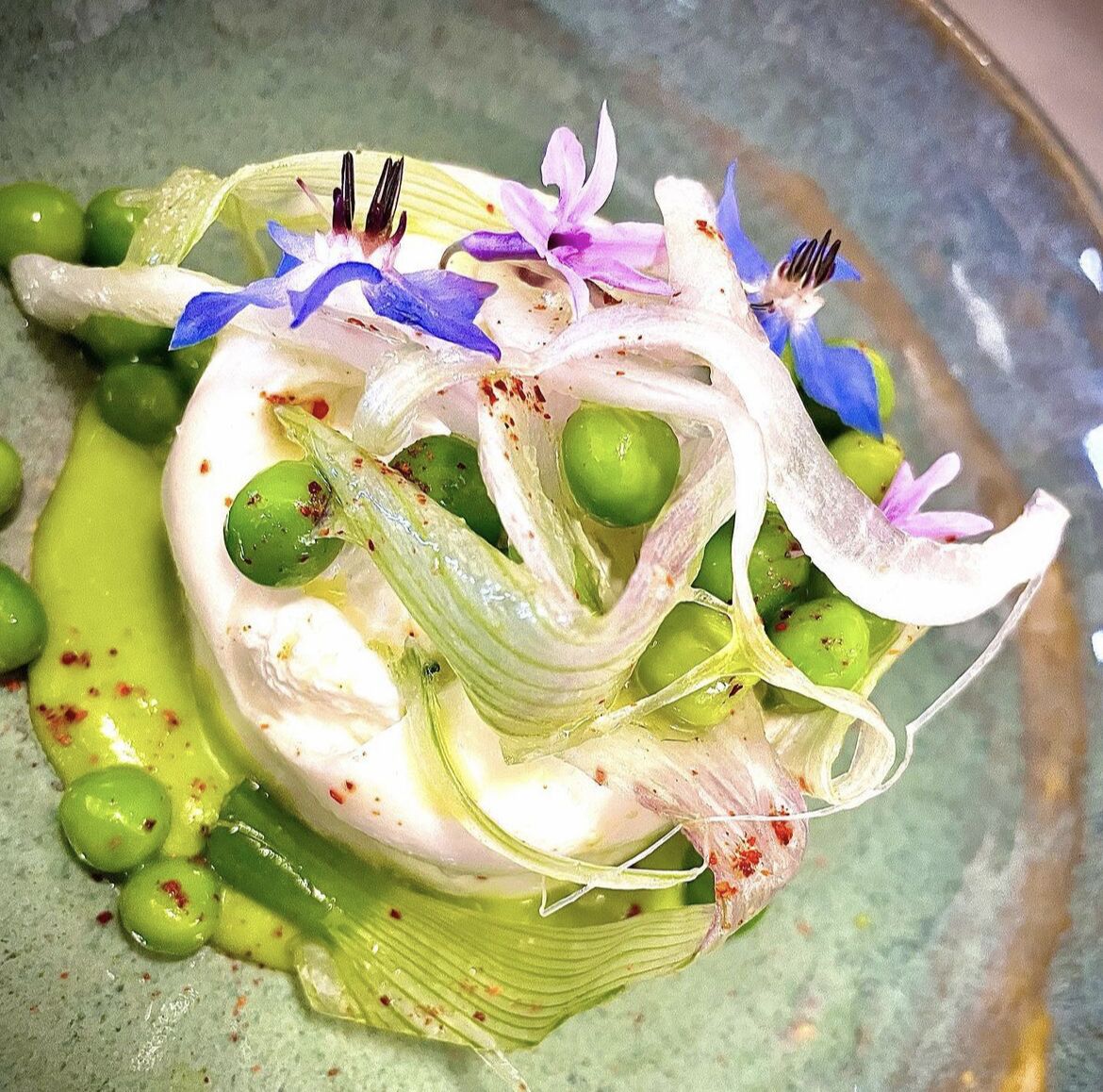 Een schotel met groene olijven, een witte, romige saus en paarse bloemen.