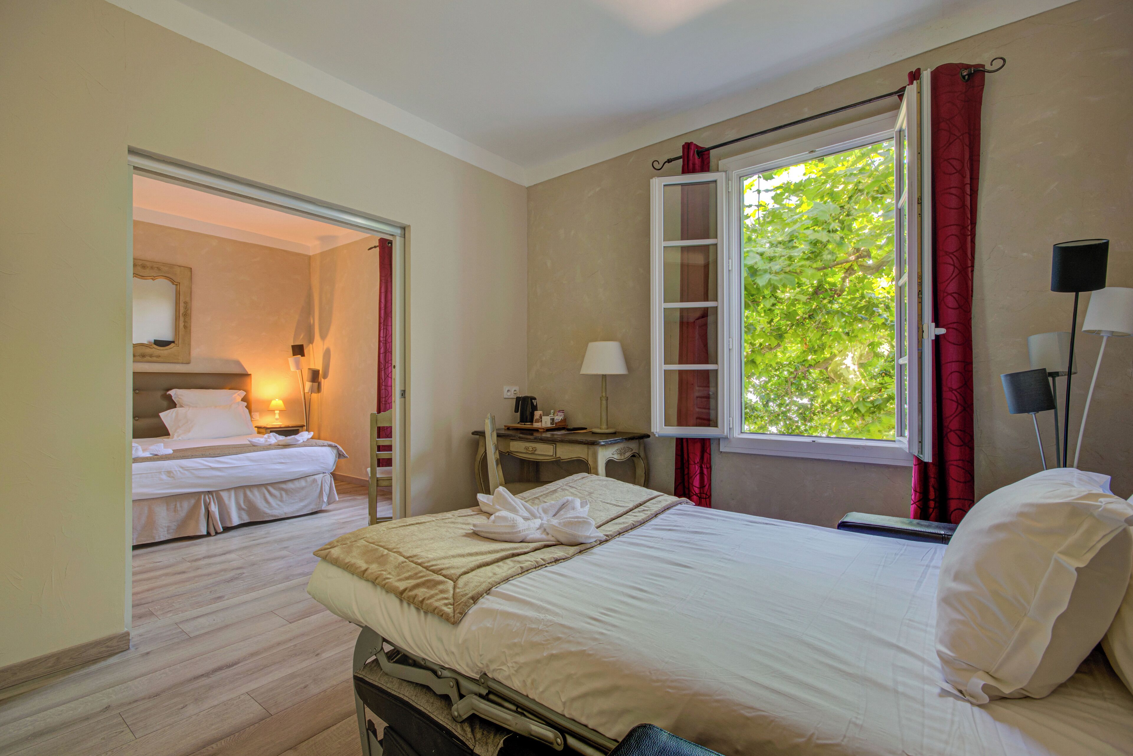 Une chambre d’hôtel avec un lit, un bureau, une chaise, une fenêtre avec des rideaux rouges et une vue sur la verdure.