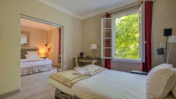 Une chambre d’hôtel avec un lit, un bureau, une chaise, une fenêtre avec des rideaux rouges et une vue sur la verdure.