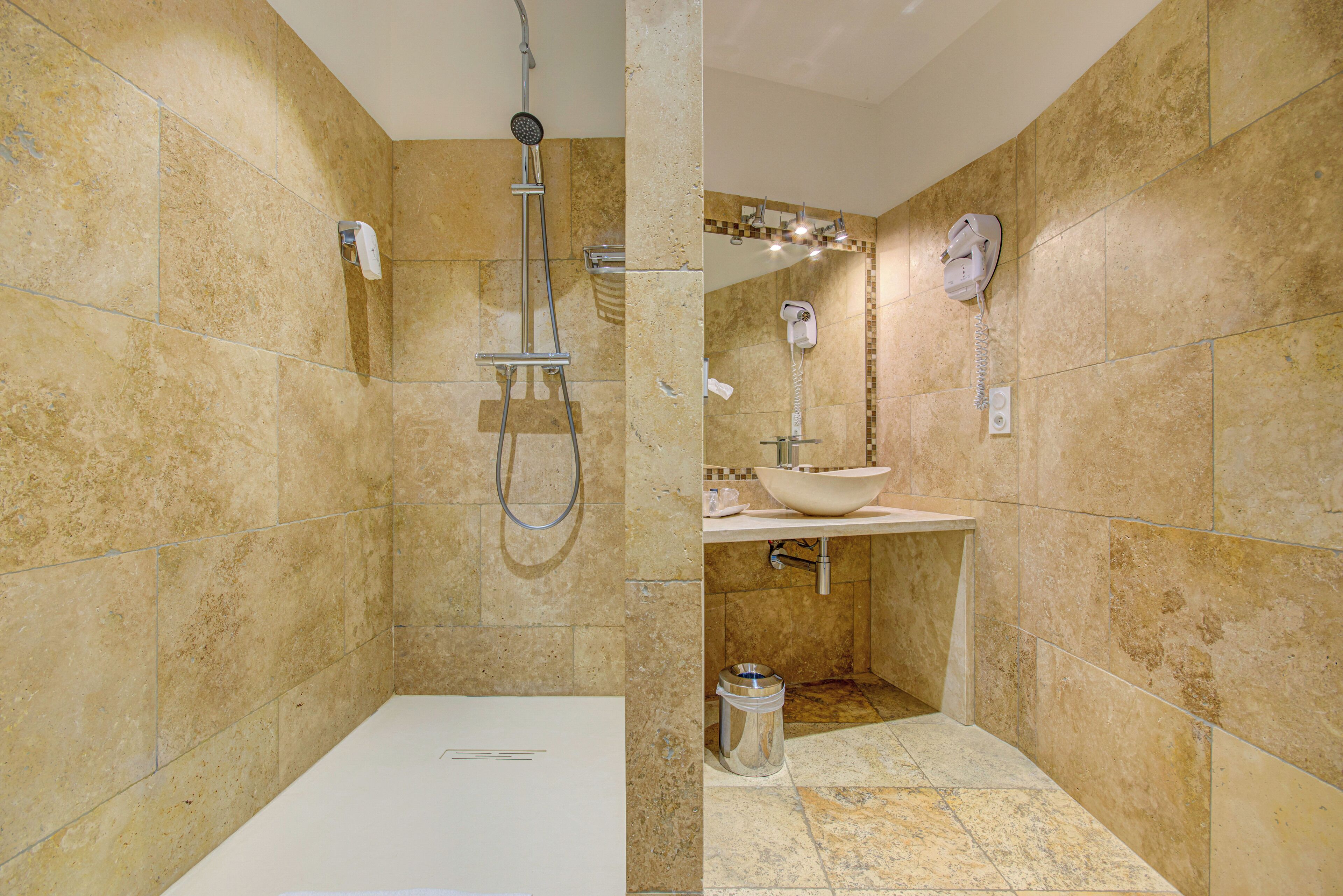 A bathroom with beige tiles, a white sink, a handheld showerhead, and a toilet.