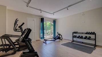 A spacious room with a treadmill, elliptical, and dumbbells on racks.