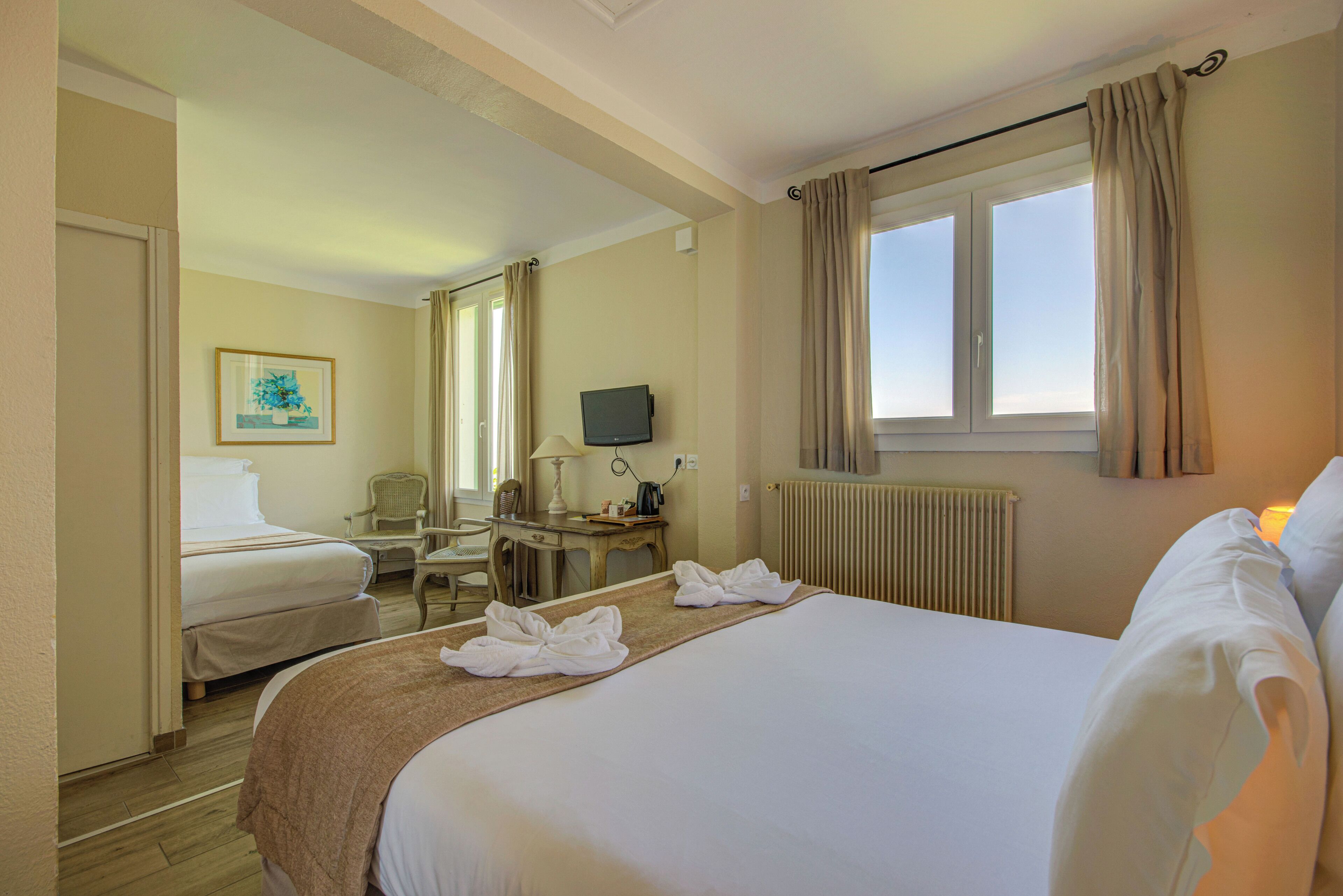 A hotel room with two beds, a desk, a chair, a television, and a window with curtains.