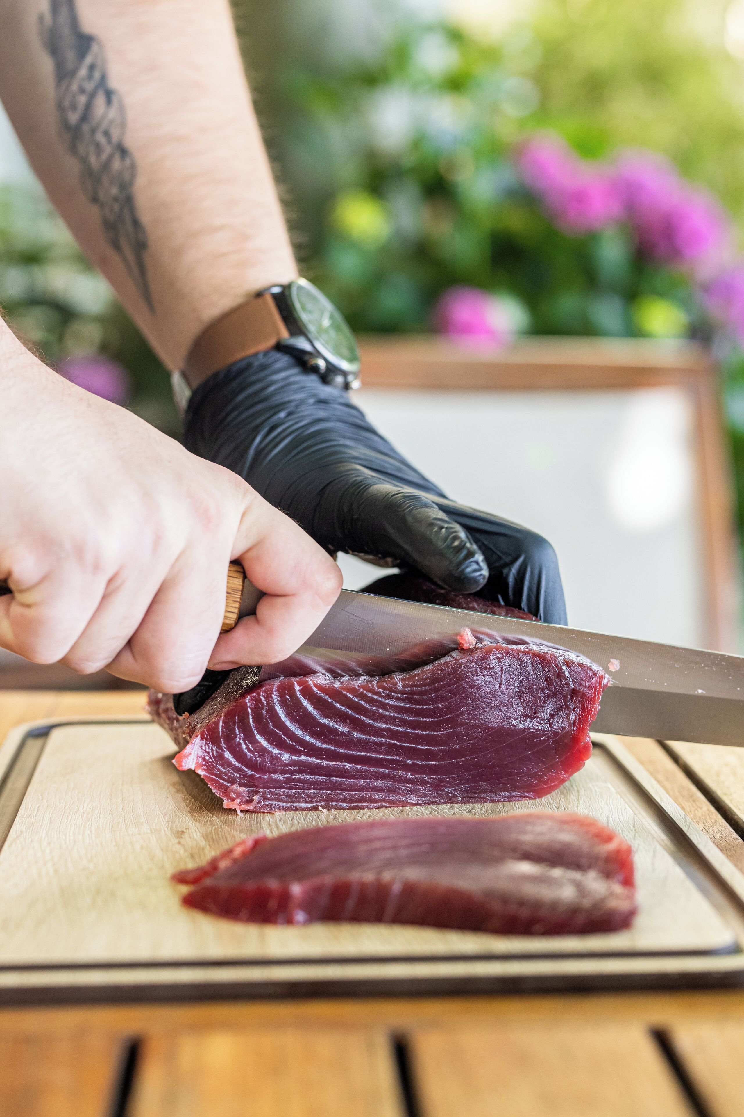 A person cutting a piece of meat on a wooden cutting board.