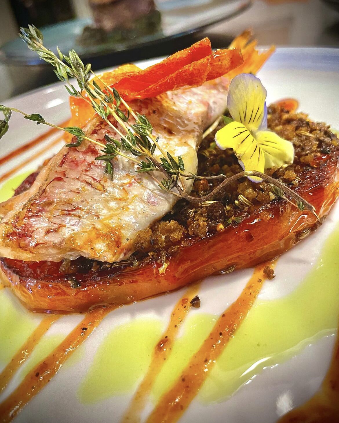 A dish with salmon, herbs, and a flower garnish on a plate with drizzled sauce.