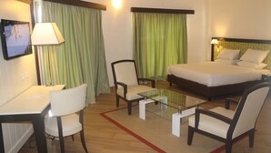 Habitación de hotel con cama, dos sillas, una mesita de cristal, escritorio y televisor.