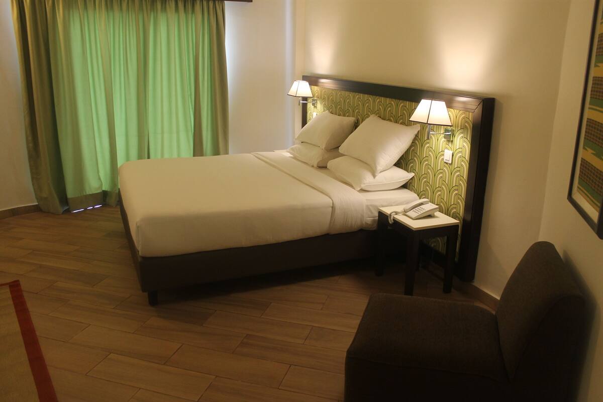 A hotel room with a bed, bedside table with a lamp, and a chair.