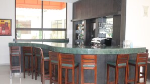 Una zona de bar con mostrador curvo, taburetes de madera y un amplio ventanal con cortina naranja.