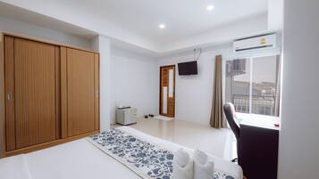 A modern hotel room with a large wardrobe, a flat-screen TV mounted on the wall, a window with a view of the city, and a small desk with a chair.