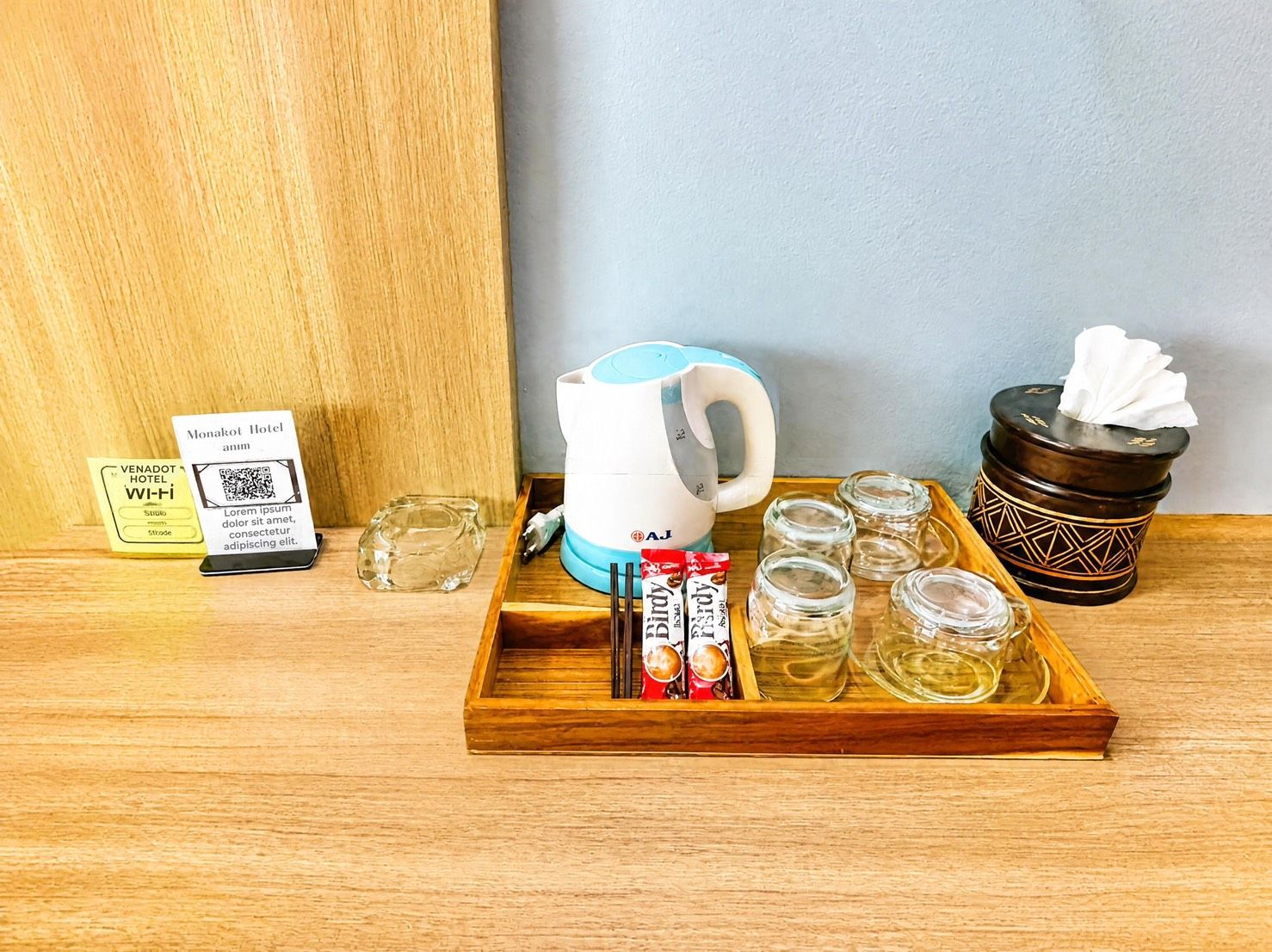 A wooden tray with a teapot, chopsticks, tea packets, and glass jars on a wooden surface.
