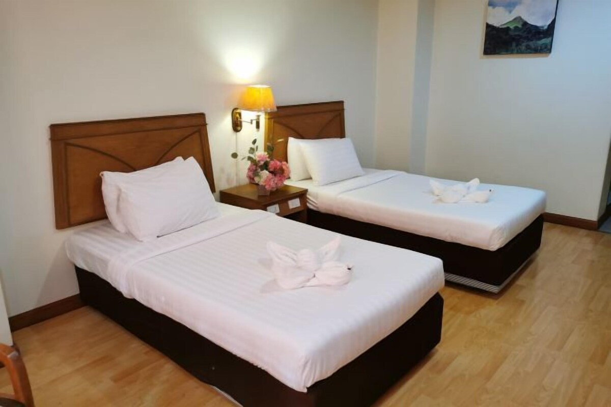 Two single beds with wooden headboards, white bedding, a nightstand with a lamp, and a painting on the wall.